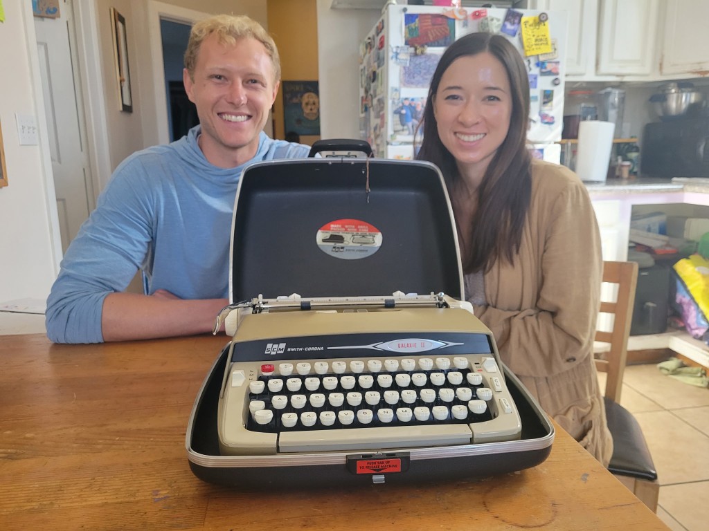 Two people at a kitchen table with a Smith-Corona Galaxie II in its open case