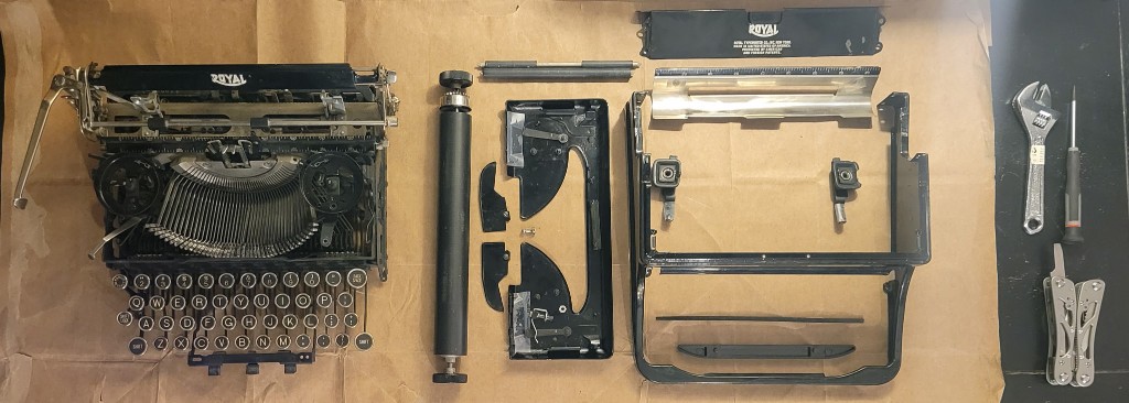 A Royal typewriter taken apart on kraft paper: chassis, platen, body, and tools laid out in a row